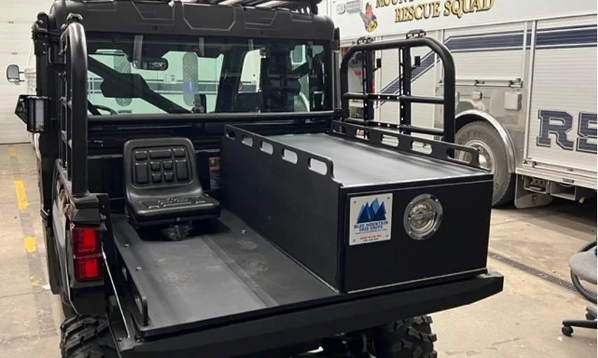 Fire department UTV carrying a Blue Mountain medical skid, parked in an apparatus bay alongside a rescue truck